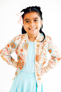 Girls retro unicorn satin jacket with floral print on cream background, worn by young girl with pink bow