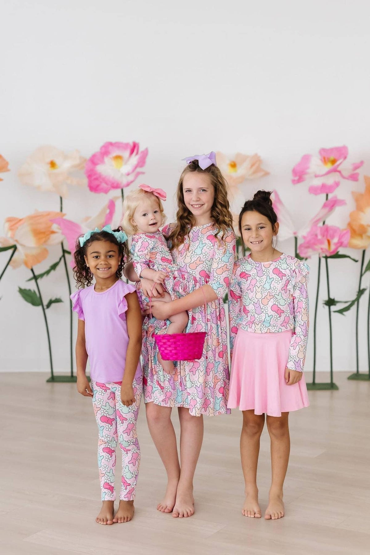 Three girls wearing girls ruffle long sleeve tee in pastel colors standing and smiling with large flower backdrop