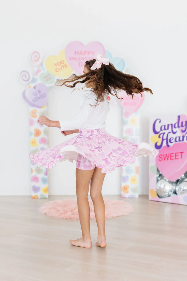 Young girl twirling in pink girls ruffle twirl skort with white top and bow in hair