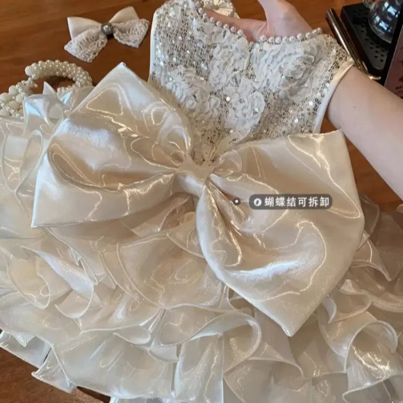 girl's white girls sequined tiered dress with large bow and lace top held by hand for babies and kids