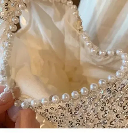 close up of white girls sequined tiered dress with pearl trim held by hand for babies and kids