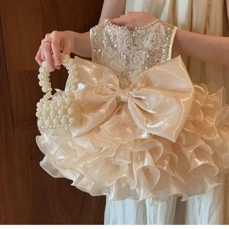 girl wearing ivory girls sequined tiered dress holding pearl handle bag close up of dress details