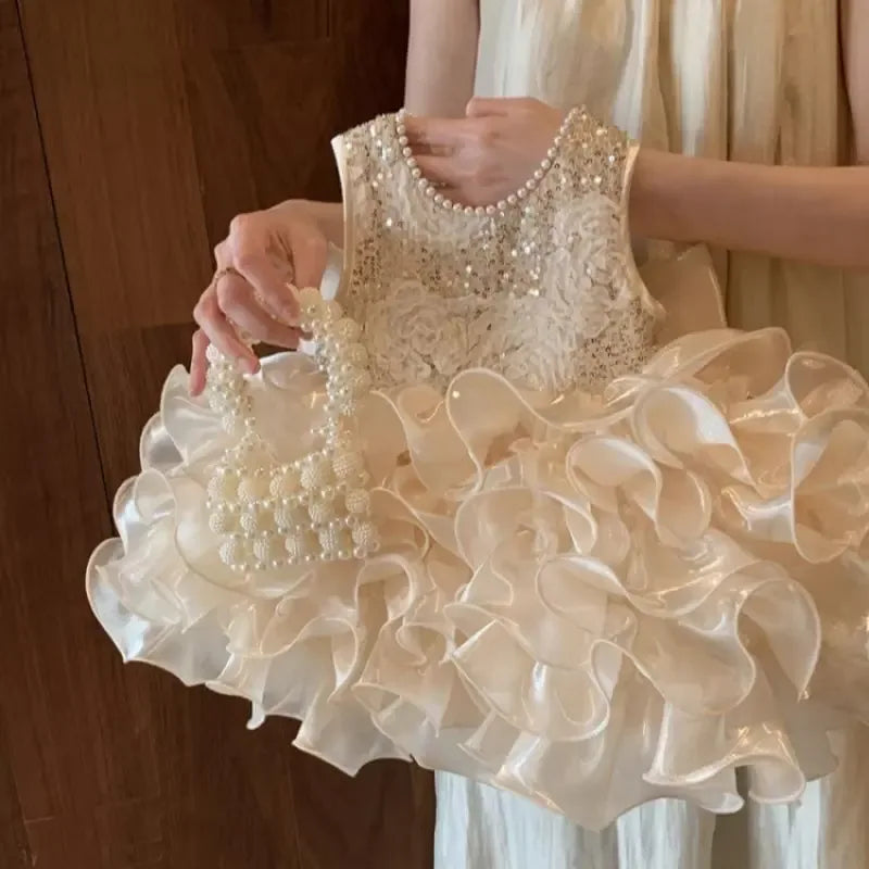 girl holding ivory girls sequined tiered dress with pearl accents and ruffled skirt