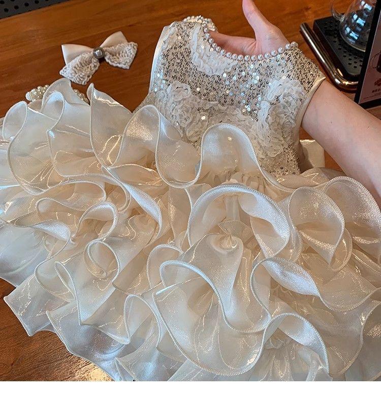 hand holding white girls sequined tiered dress with ruffled skirt and matching bow headband
