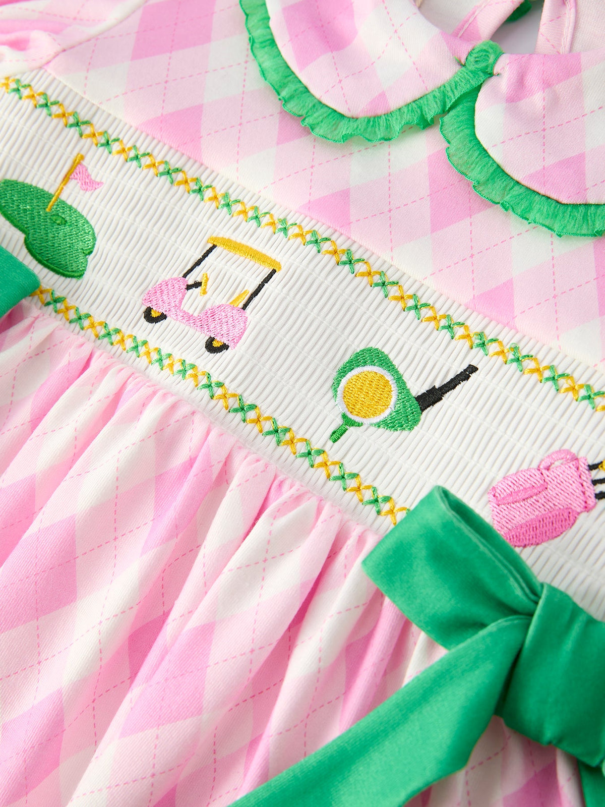 Close-up of pink and white girls smocked golf dress with green bow and golf-themed embroidery