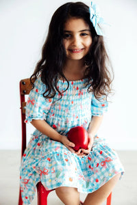 Girls smocked ruffle dress by Mila & Rose in light blue with bow print, worn by young girl with matching hair bow