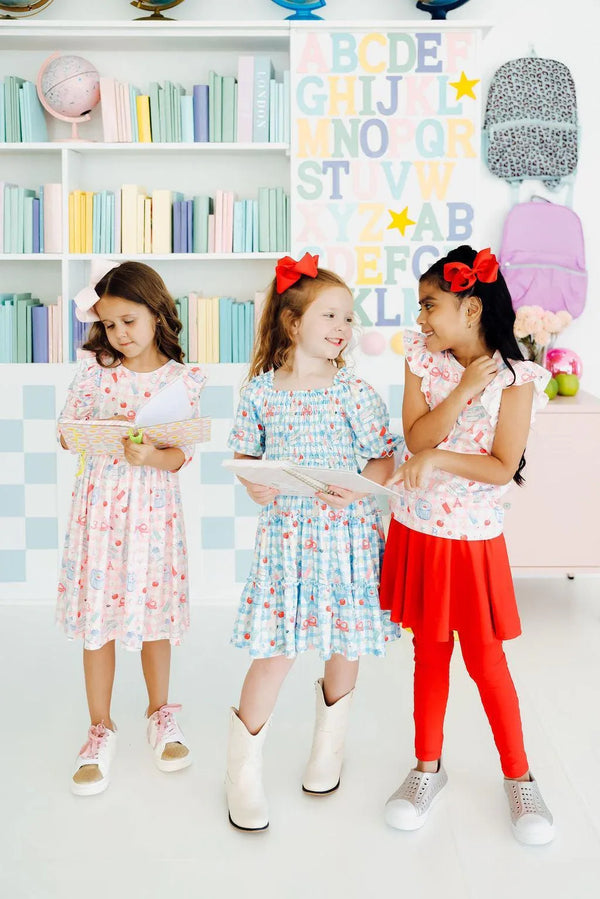 Three girls wearing colorful girls smocked ruffle dresses in white and blue with floral prints, sizes for kids
