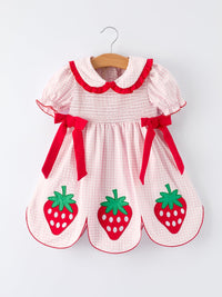 Pink and white girls strawberry smocked dress with red bows and strawberry appliques hanging on wooden hanger