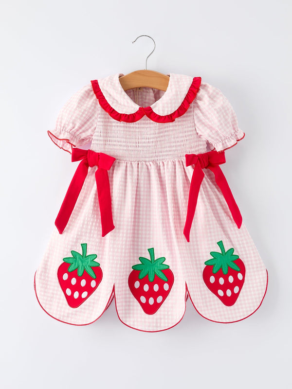 Pink and white girls strawberry smocked dress with red bows and strawberry appliques hanging on wooden hanger