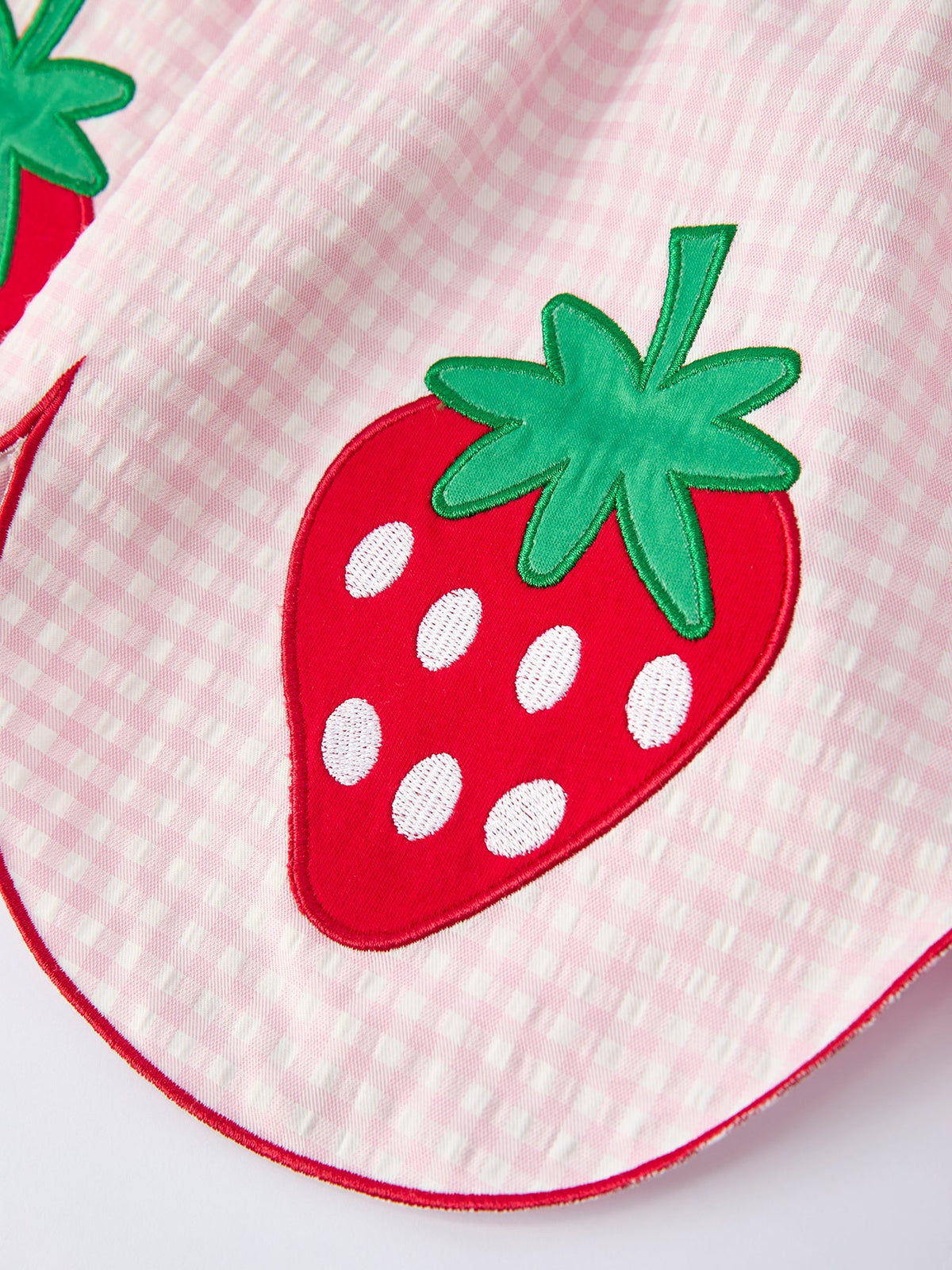 Close-up of pink gingham girls strawberry smocked dress with red and green strawberry applique