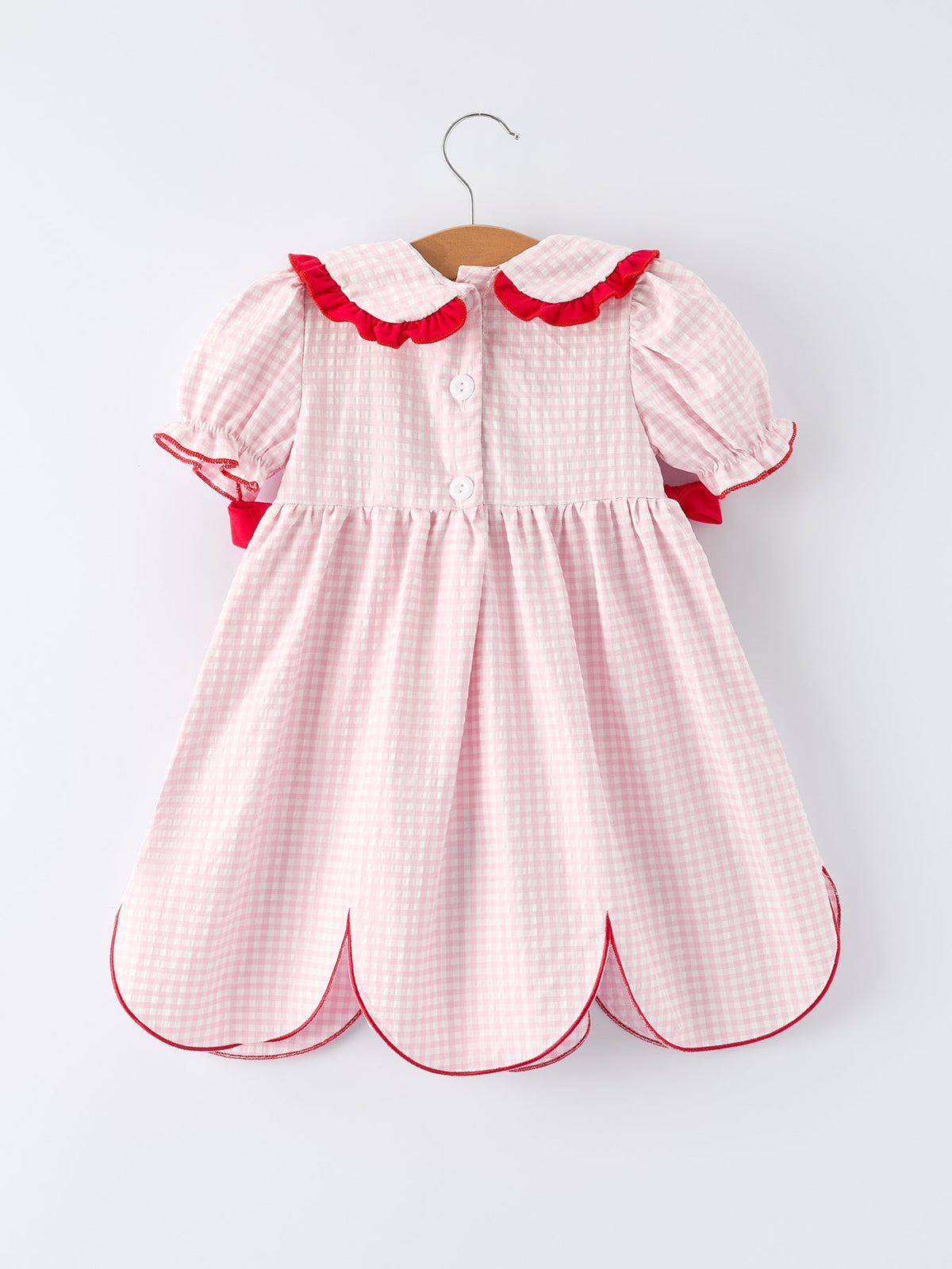 pink and white girls strawberry smocked dress with red trim hanging on wooden hanger