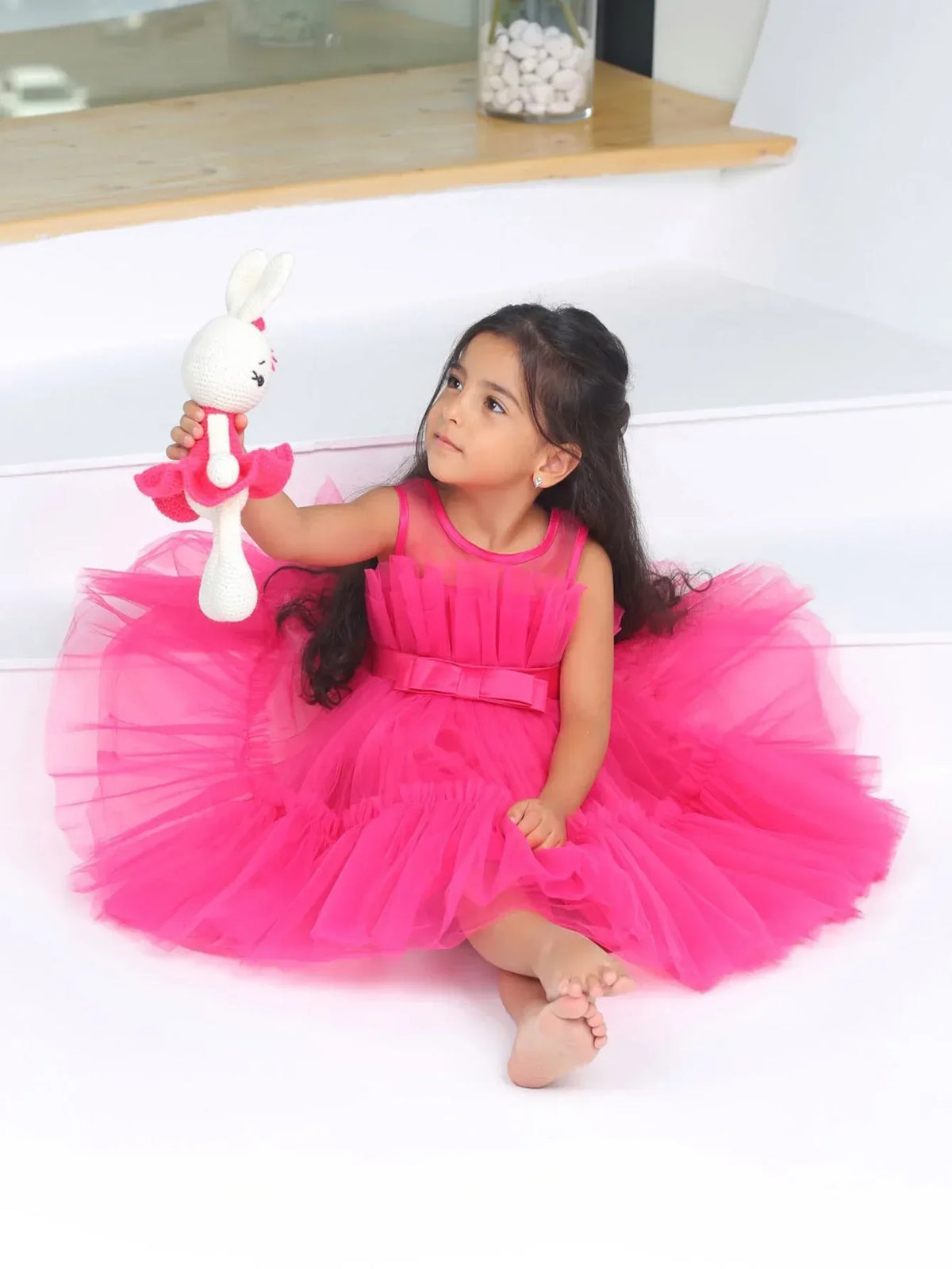 Bright pink girls tulle occasion dress with sleeveless bodice worn by toddler holding a stuffed bunny