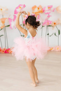 Young girl wearing pink Mila & Rose girls tutu leotard twirling with arms raised in dance pose