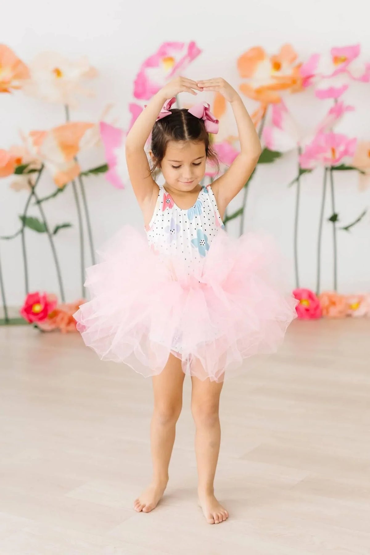 Young girl wearing pink girls tutu leotard standing in ballet pose with arms overhead
