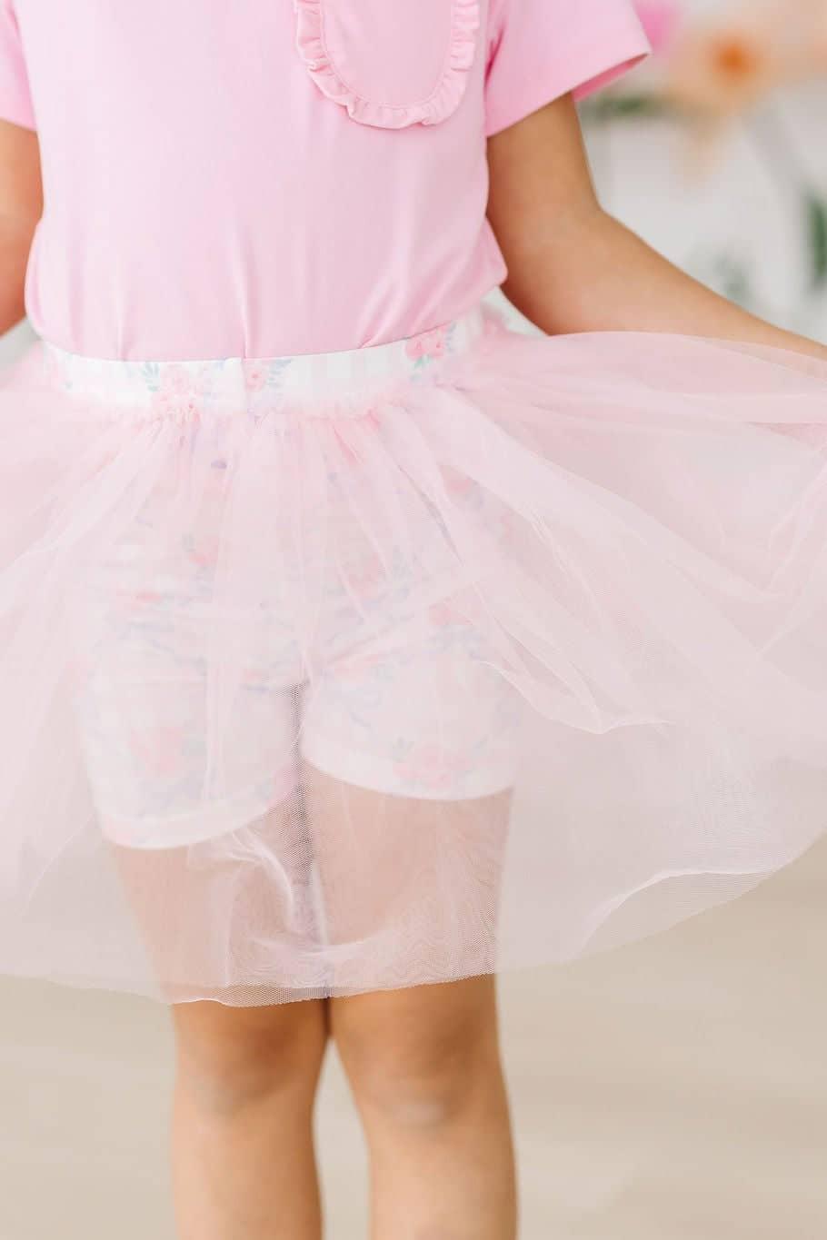 Young girl wearing light pink girls tutu shorts holding out skirt with both hands