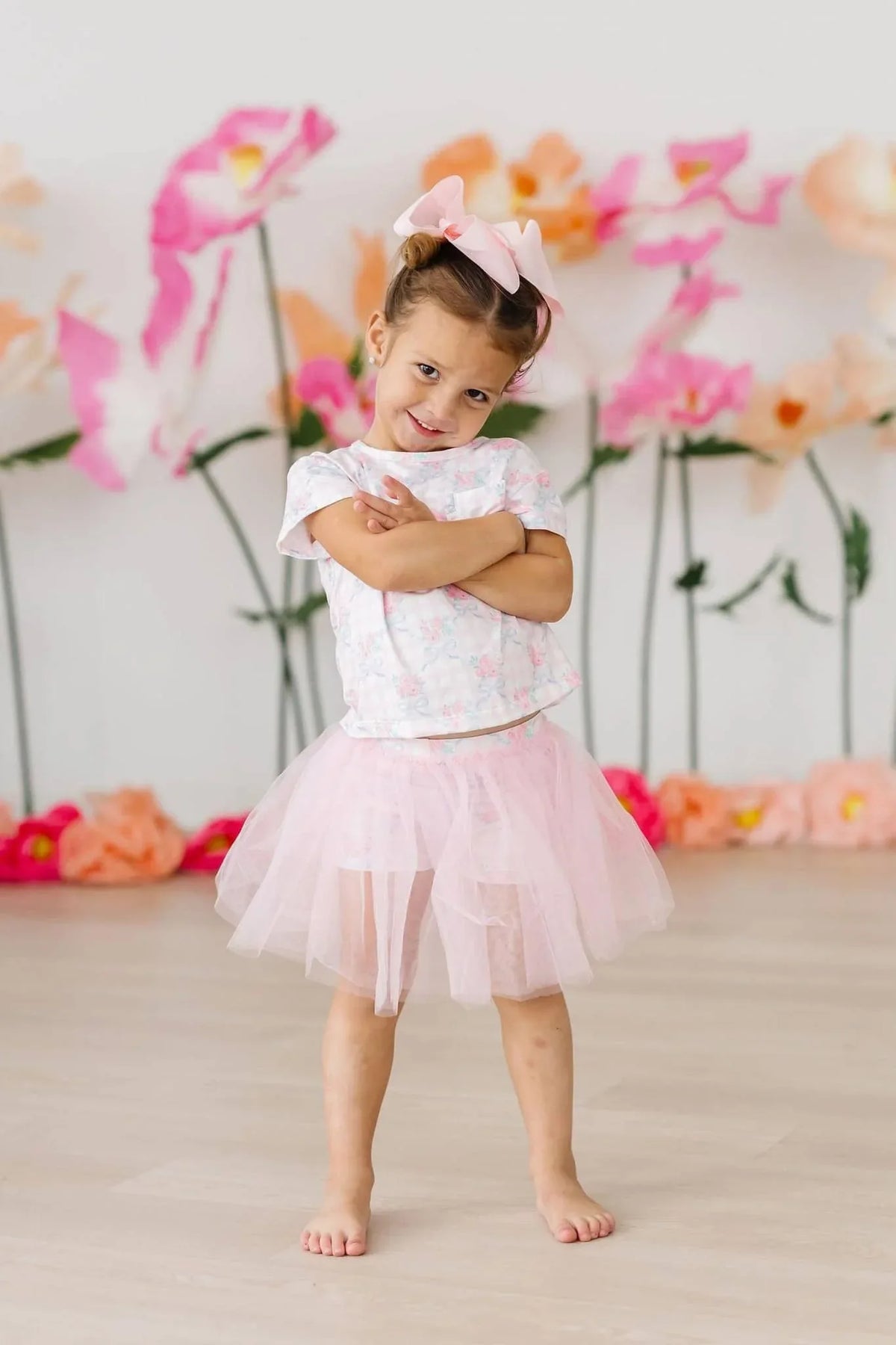 toddler girl wearing pink Mila & Rose girls tutu shorts standing with arms crossed in front of floral backdrop