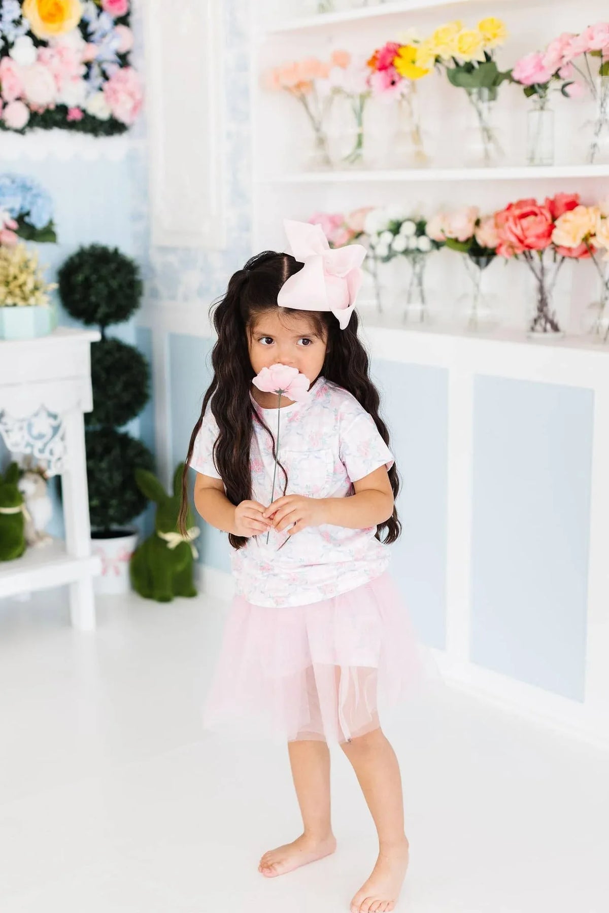 Young girl wearing pink girls tutu shorts and matching bow holding a flower in a floral room