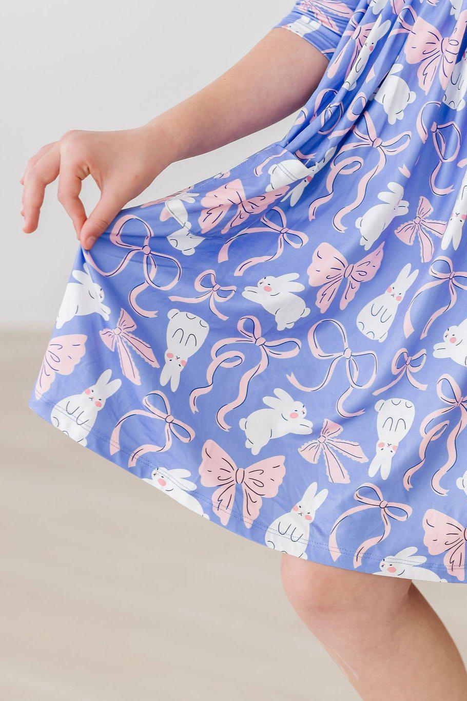 Girl wearing blue Mila Rose girls twirl dress with pockets holding skirt with white bunnies and pink bows