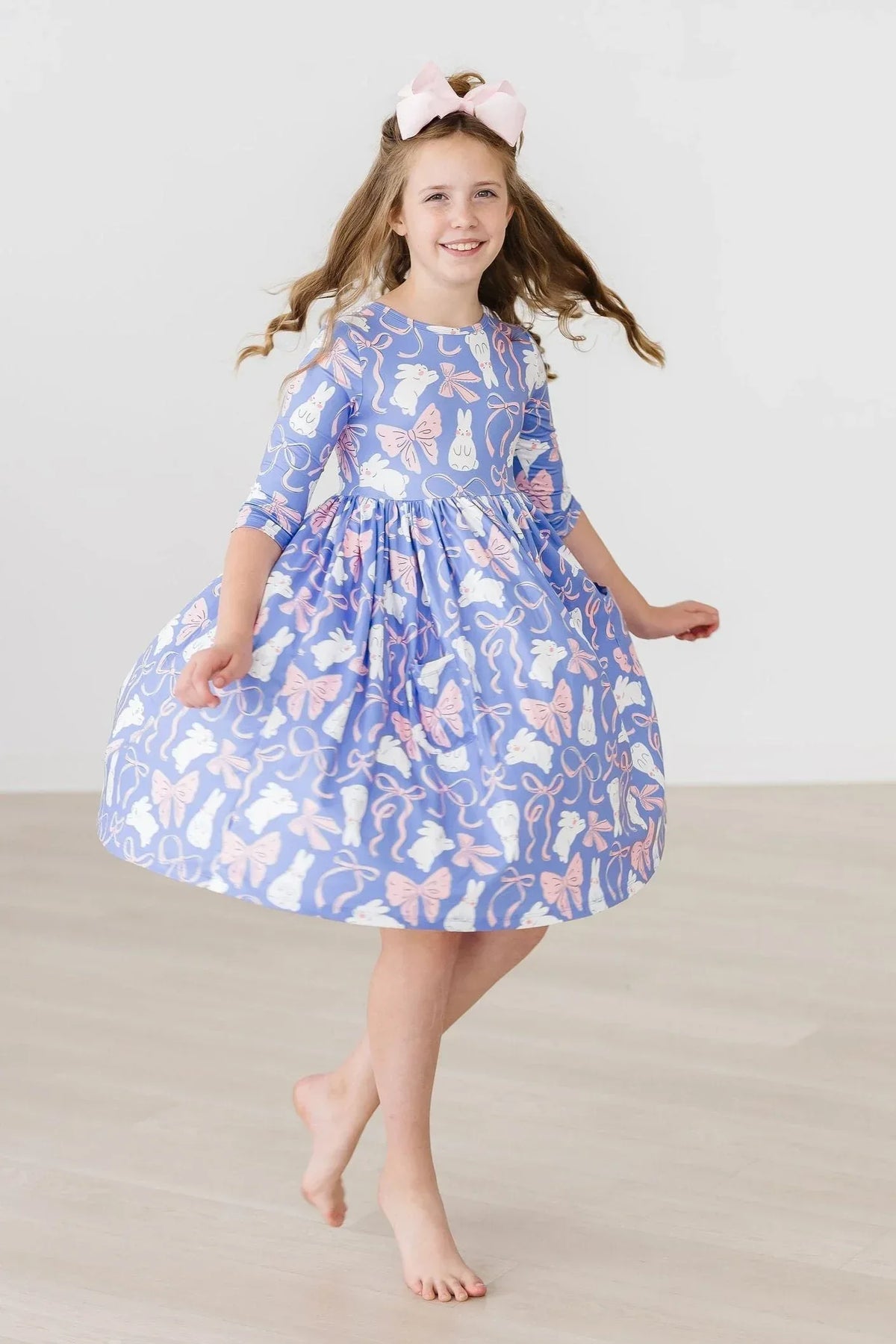 Young girl wearing blue Mila & Rose girls twirl dress with pockets spinning barefoot indoors