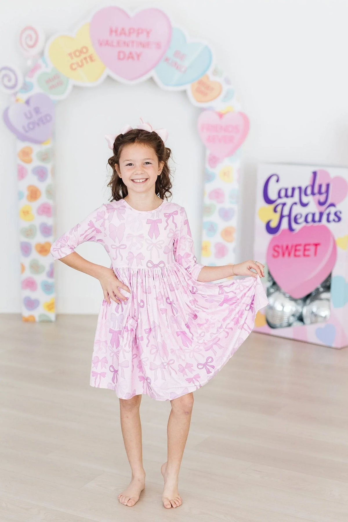 Smiling girl wearing pink Mila & Rose girls twirl dress with pockets holding dress hem and posing indoors