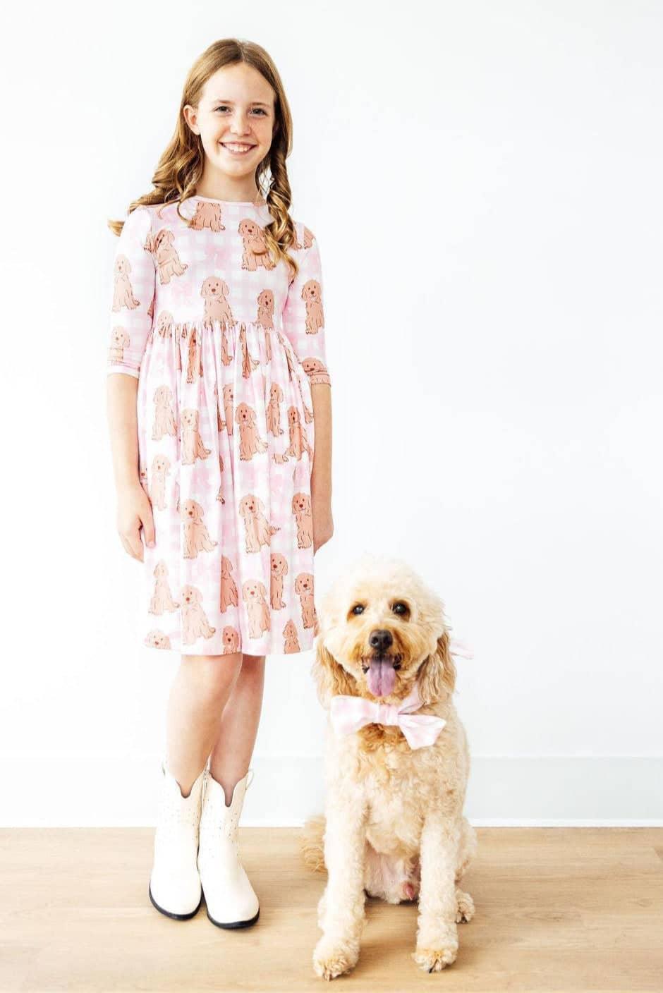 Girl wearing pink goldendoodle twirl dress for girls standing next to a goldendoodle dog with matching bow tie