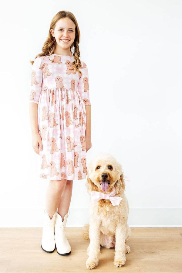 Girl wearing pink goldendoodle twirl dress for girls standing next to a goldendoodle dog with matching bow tie