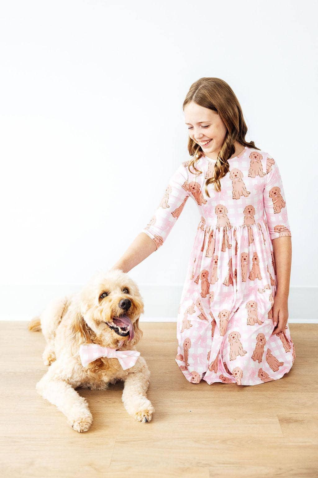 Girl wearing pink goldendoodle twirl dress for girls smiling and petting a goldendoodle dog