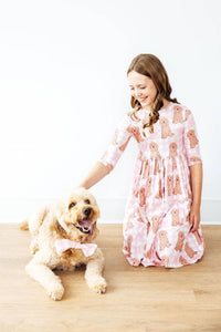 Girl wearing pink goldendoodle twirl dress for girls smiling and petting a goldendoodle dog