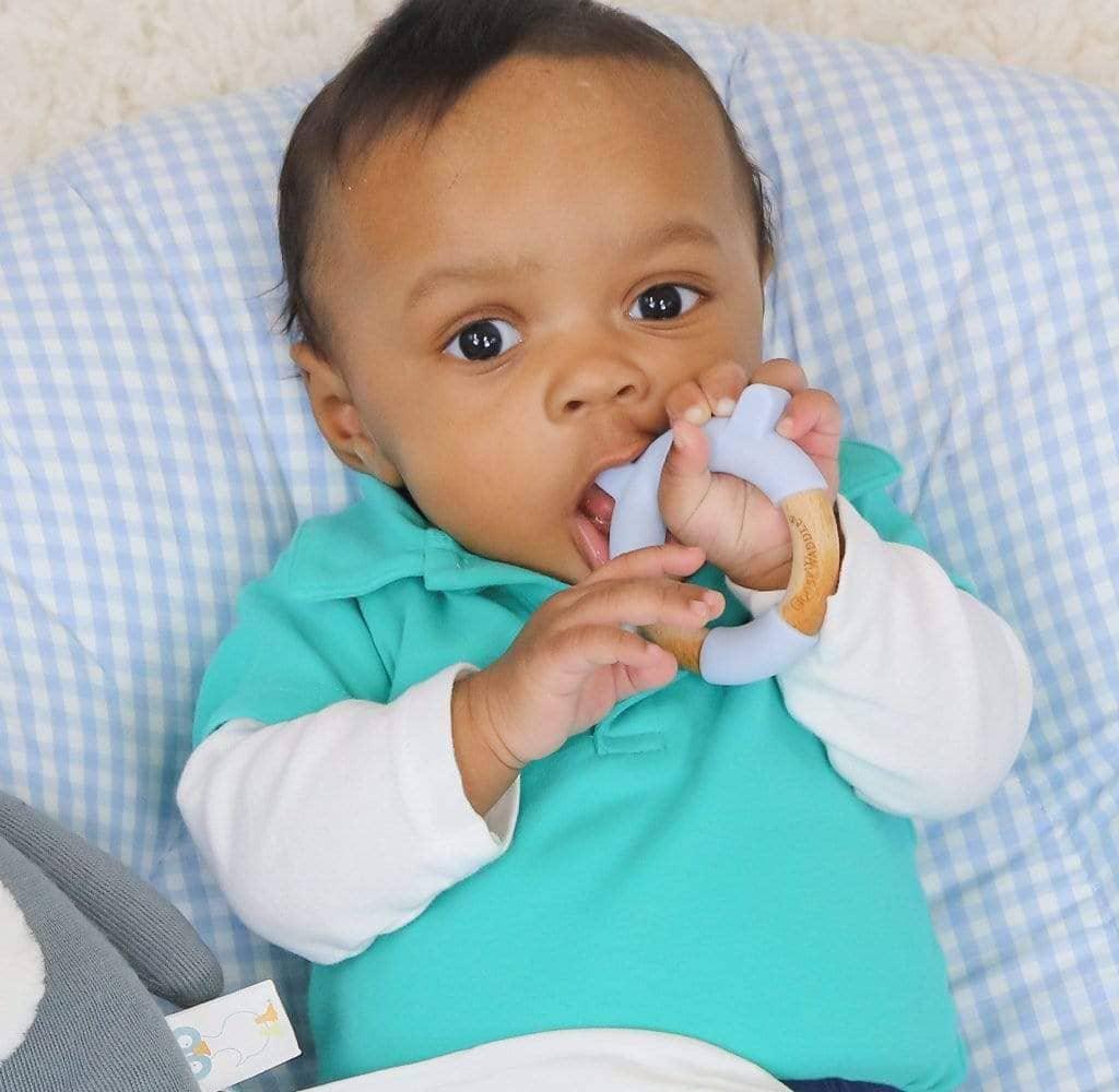 Baby holding and chewing a blue bear teether made of soft silicone and natural wood