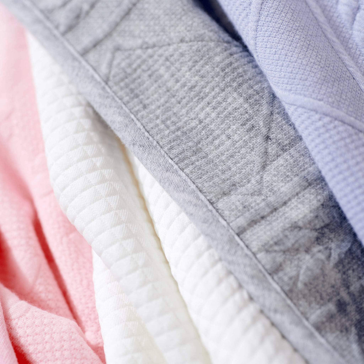 Soft gray knit baby blanket folded alongside pink and white blankets for newborns