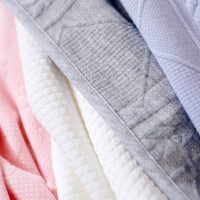 Soft gray knit baby blanket folded alongside pink and white blankets for newborns