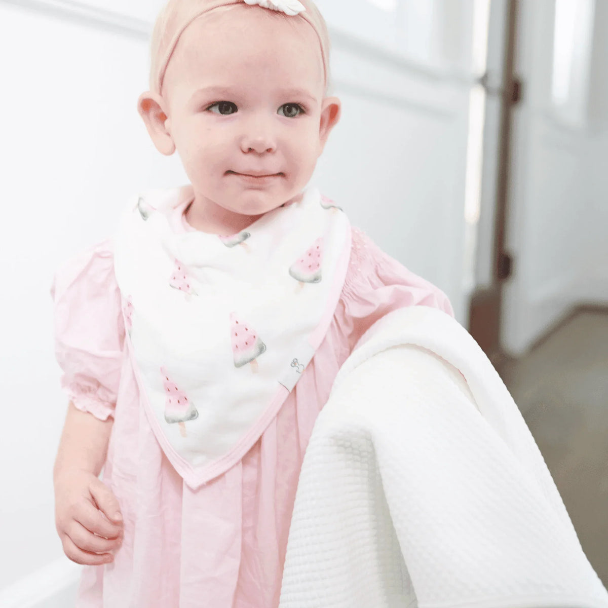 Soft white baby knit blanket made of cozy material held by a baby girl in pink dress