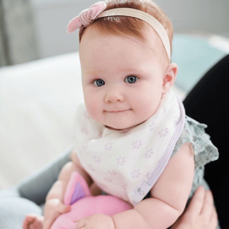 Adorable baby wearing the Blueberries and Flowers Lavender 2 Pack Muslin & Terry Cloth Bib Set, showcasing a stylish lavender design, holding a plush toy in a cozy setting.