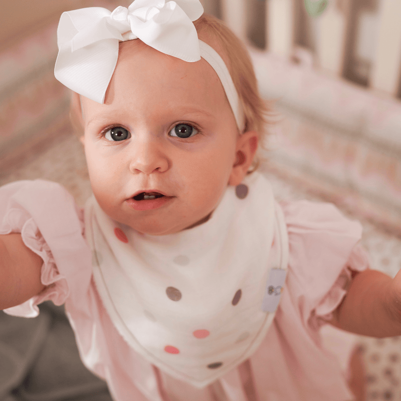A cheerful baby wearing the Mom and Dots 2 Pack Muslin & Terry Cloth Bib Set, showcasing its playful design with polka dots. The bib is soft and absorbent, perfect for keeping your little one clean during meals.