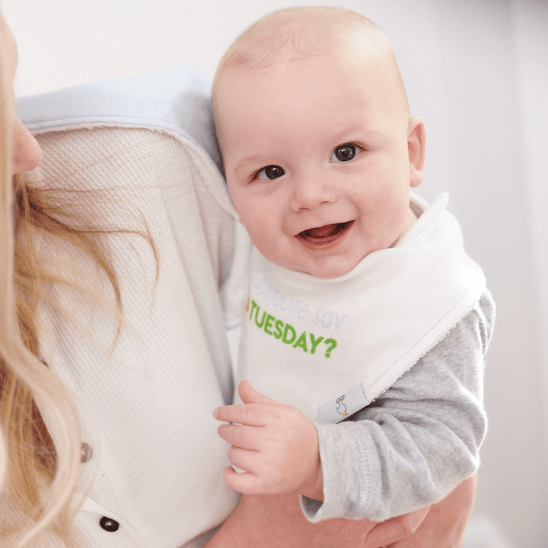 Happy baby wearing the Taco Tuesday and Taco 2 Pack Muslin & Terry Cloth Bib Set, smiling while being held, showcasing comfort and style during mealtime.