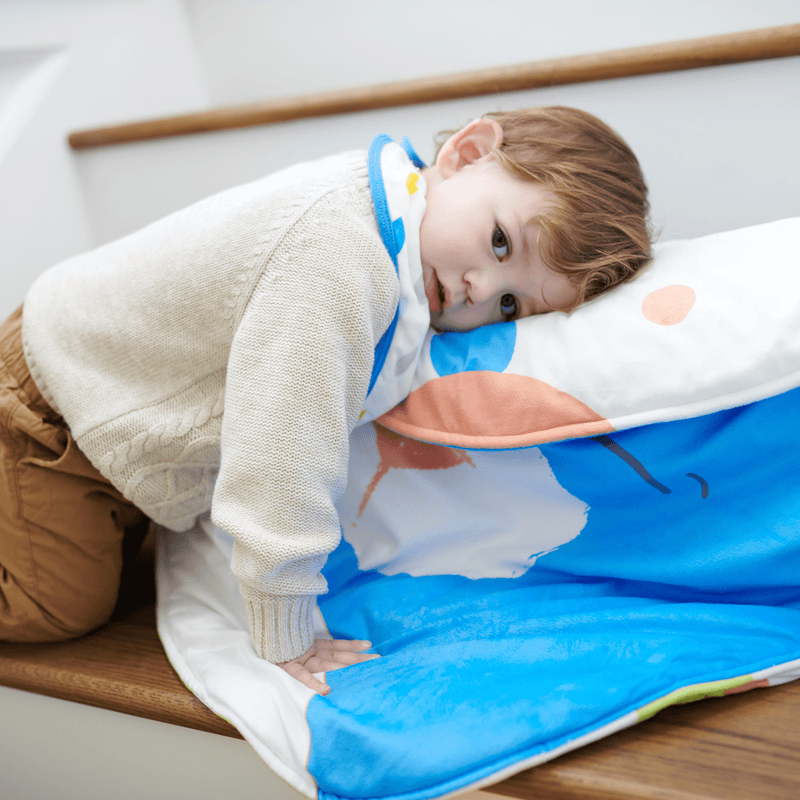 A child relaxing on the Bear Stroller Blanket from Goosewaddle®, showcasing its playful design and comfort suitable for cozy moments.