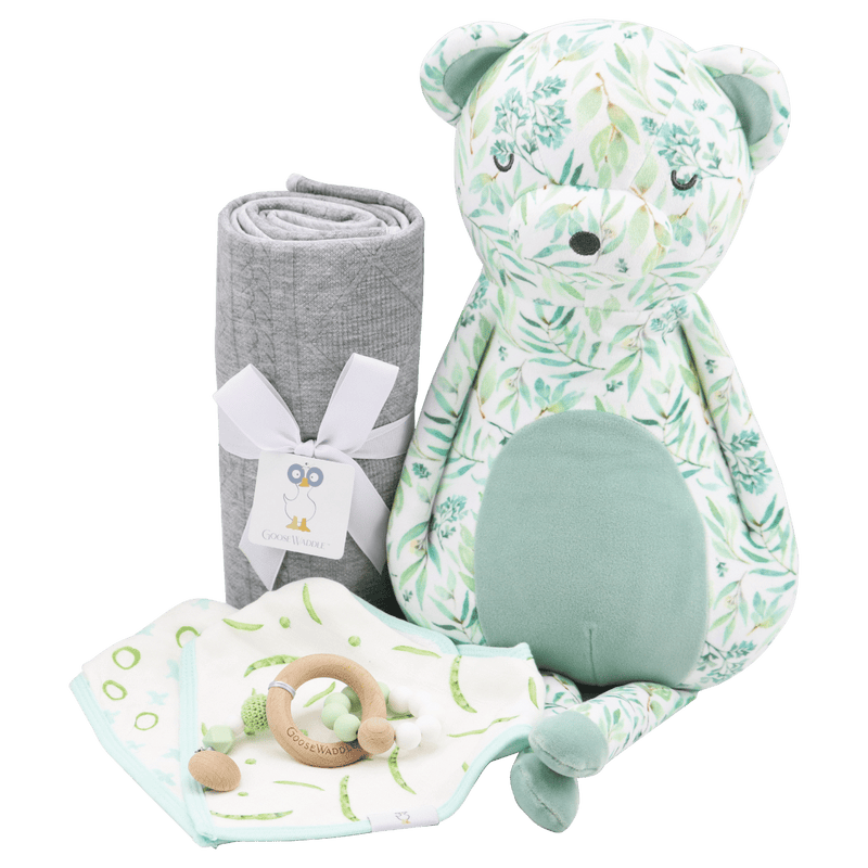 Gray Knit Blanket by Goosewaddle® accompanied by a plush bear toy and other baby essentials. The blanket is soft and features a chic gray design, perfect for cozying up in a nursery.