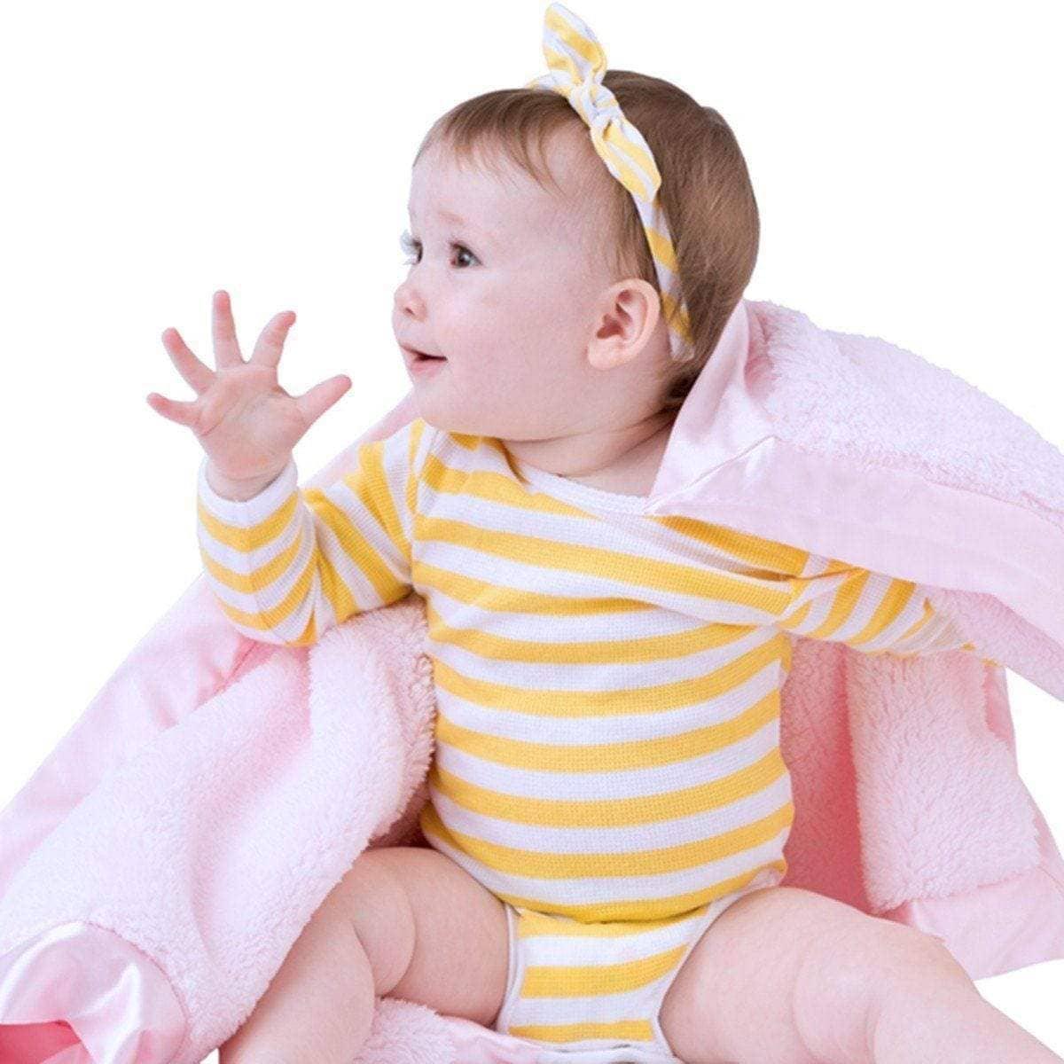 baby girl wearing yellow striped onesie wrapped in pink luxury baby blanket satin trim reaching out
