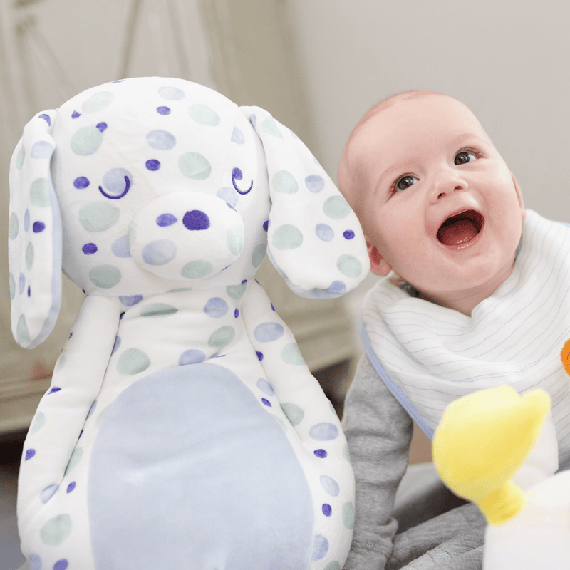Happy baby smiling next to a Super Soft Printed Plush, featuring colorful polka dots, perfect for cuddling and playtime.