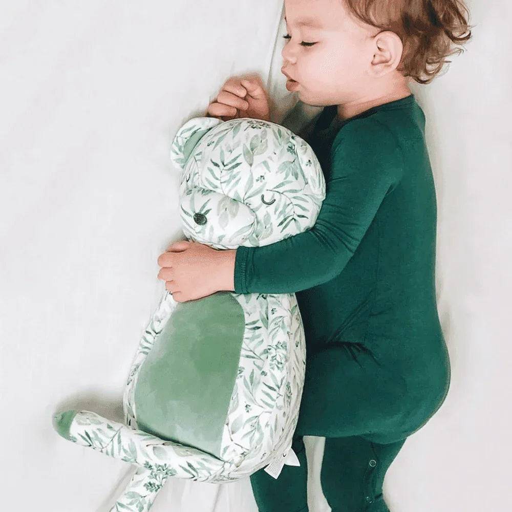 baby in green pajamas hugging mint plush bear for babies with leafy print lying down