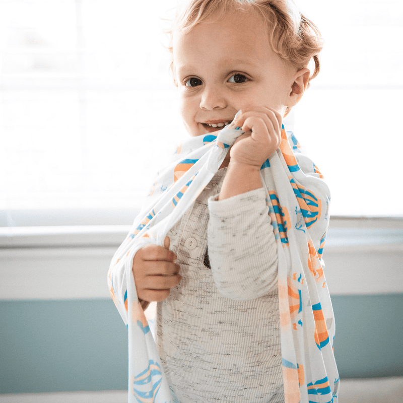 2 PK Newborn Receiving Blankets by Goosewaddle® featuring a joyful toddler playfully wrapped in a colorful blanket, perfect for fun and comfort.