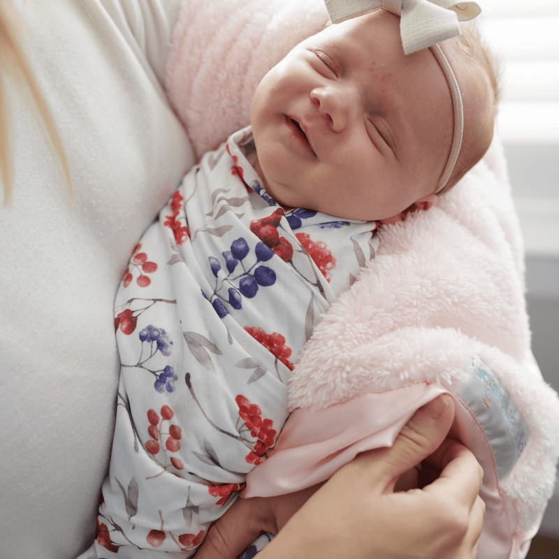 2 PK Newborn Receiving Blankets by Goosewaddle® highlighting a joyful baby swaddled in floral designs, offering warmth during cuddles.