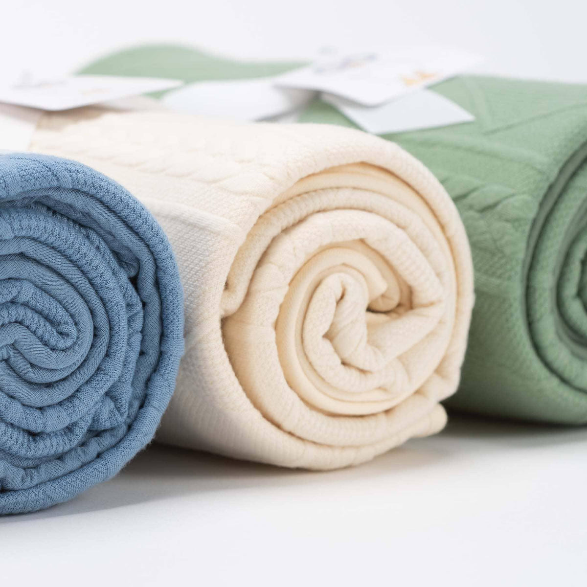 Rolled oatmeal knit baby blanket for newborns displayed alongside blue and green knit baby blankets