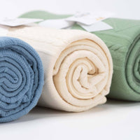 Rolled oatmeal knit baby blanket for newborns displayed alongside blue and green knit baby blankets