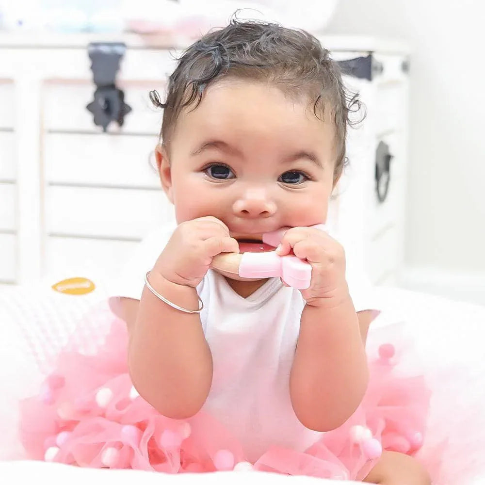 Baby holding soft silicone and wood pink bunny teether while wearing pink tutu dress