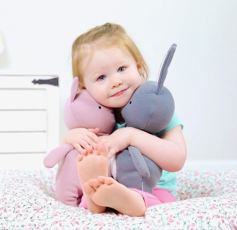 A smiling young child happily hugging two plush toys, including the Pig Knit Plush, showcasing its charm and comfort alongside a bunny toy.