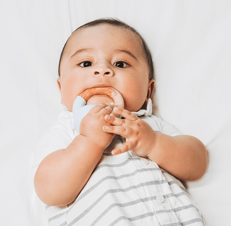 Happy baby enjoying the Rattle Teether Wooden + Silicone, grasping the teething toy with both hands, showcasing its engaging design for soothing tender gums.