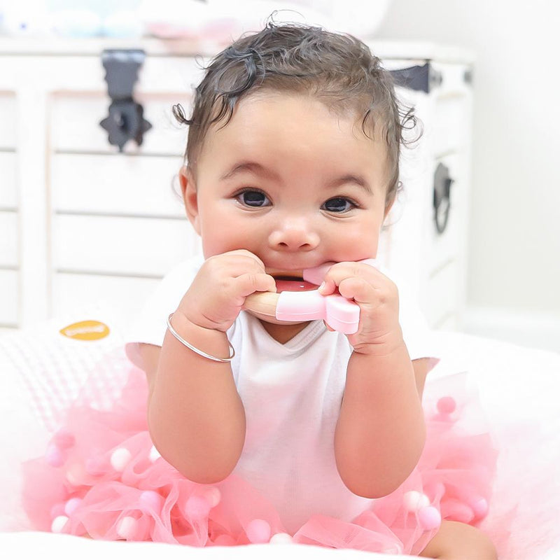 A happy baby wearing a pink tutu holds the Pink Bunny Circle Bunny Head Teether made of wood and silicone, enjoying teething relief.