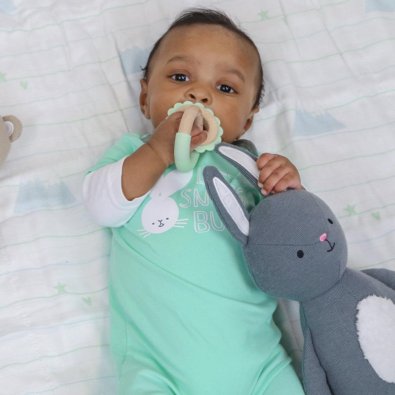 A baby comfortably holding the Mint Lion Silicone + Wood Double Teether, promoting teething relief while enjoying safe playtime with a plush toy.