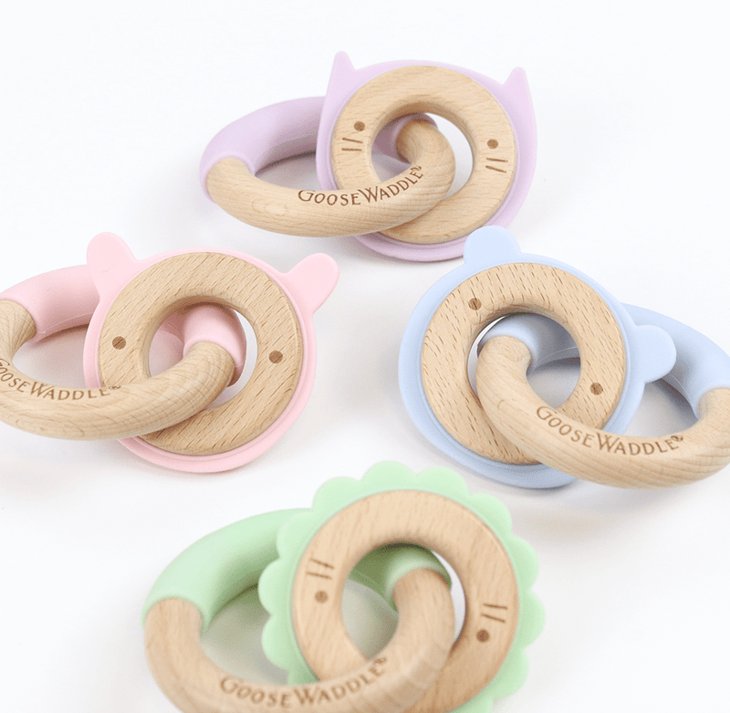 Various Gooswaddle teething rings, including the Mint Lion Silicone + Wood Double Teether, highlighting colorful silicone designs and natural wood accents.